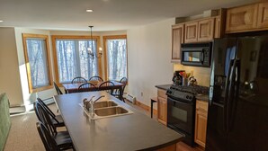 A modern kitchen with a central island, wooden cabinets, a black refrigerator, and a dining area with chairs and a table.