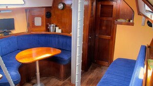 Ein kompakter Innenraum mit einer blauen Sitzgelegenheit mit Polstern, einem kleinen Holztisch und einer Holztür.