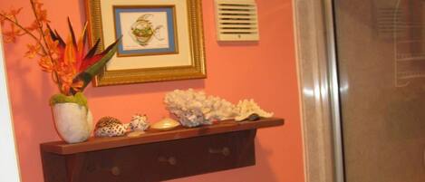 A bathroom with a toilet, a shower enclosure, a shelf with decorative items, and a framed picture on the wall.