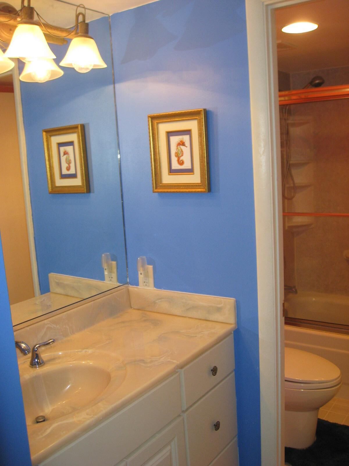 A bathroom with a blue wall, a white sink with a marble countertop, and two framed pictures above the mirror.