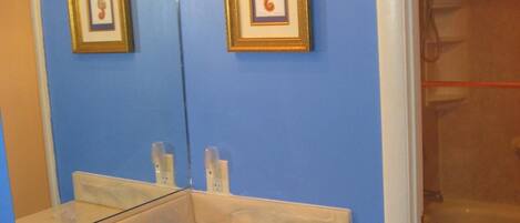 A bathroom with a blue wall, a white sink with a marble countertop, and two framed pictures above the mirror.
