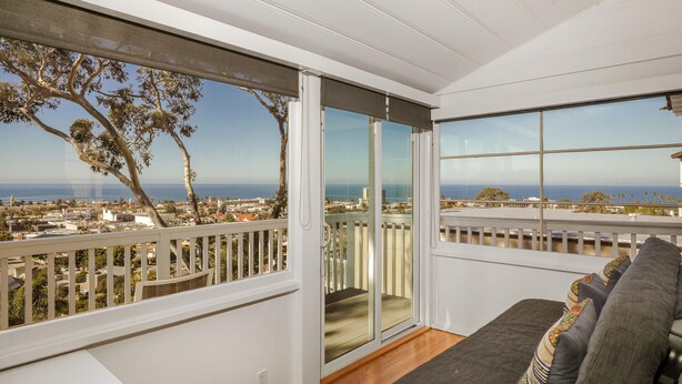 A balcony with a view of the ocean and cityscape, a sliding glass door, and a sofa with patterned cushions. - Stunning Oceanview Craftsman in the village Of La Jolla - Walk To All! (San Diego)