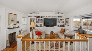 A spacious living room with a fireplace, a large TV, and a bookshelf filled with books. - Stunning Oceanview Craftsman in the village Of La Jolla - Walk To All! (San Diego)