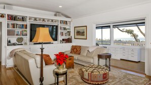 A living room with a sofa, ottoman, lamp, and a bookshelf filled with books. - Stunning Oceanview Craftsman in the village Of La Jolla - Walk To All! (San Diego)