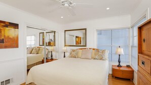 A bedroom with a large bed, two bedside tables with lamps, a ceiling fan, a large mirror, and a window with blinds. - Stunning Oceanview Craftsman in the village Of La Jolla - Walk To All! (San Diego)