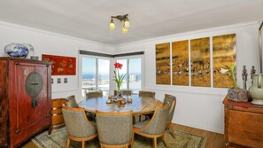Ein Esszimmer mit einem runden Tisch, sechs Stühlen, einem roten Schrank und Blick auf das Meer durch große Fenster.