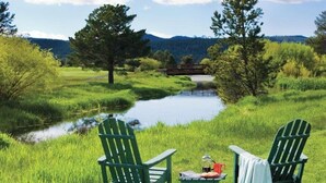 A serene outdoor setting with two Adirondack chairs, a small table with a book and a cup, and a bridge in the background.