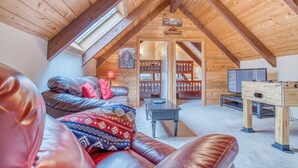 A cozy loft-style room with a sloped ceiling, a wooden ceiling fan, a sofa with patterned cushions, a small table, and a wooden foosball table.