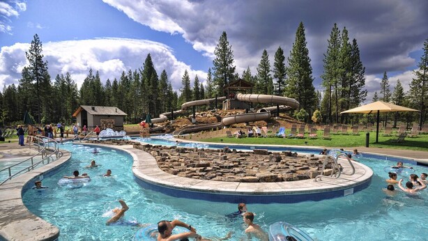 A swimming pool with multiple lanes, a water slide, and a surrounding wooded area.