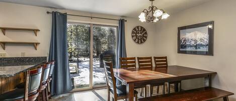 Un comedor con una mesa y sillas de madera, un banco, una araña, un reloj y un cuadro en la pared.
