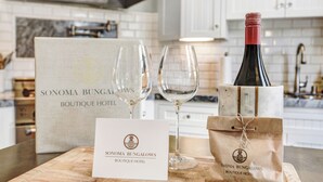 Ein Holztisch mit einer Weinflasche, zwei Weingläsern, einer Speisekarte und einer Papiertüte mit dem Logo vom Sonoma Bungalows Boutique Hotel.