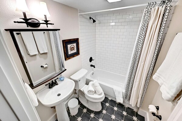 A bathroom with a white sink, toilet, and bathtub. There is a framed picture on the wall and a shower curtain with a pattern. - Renovated 3BA/2BD Condo 2 Miles from Downtown (Austin)