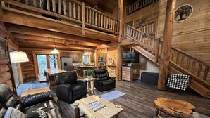 Ein rustikales Blockhaus mit Wohnzimmer, Essbereich, Küche und einer Treppe.