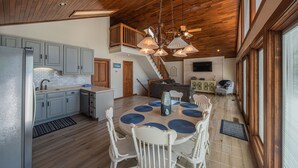 Une cuisine spacieuse avec des meubles de rangement en bois, un coin repas avec une table ronde et des chaises, et un escalier menant à l’étage supérieur.