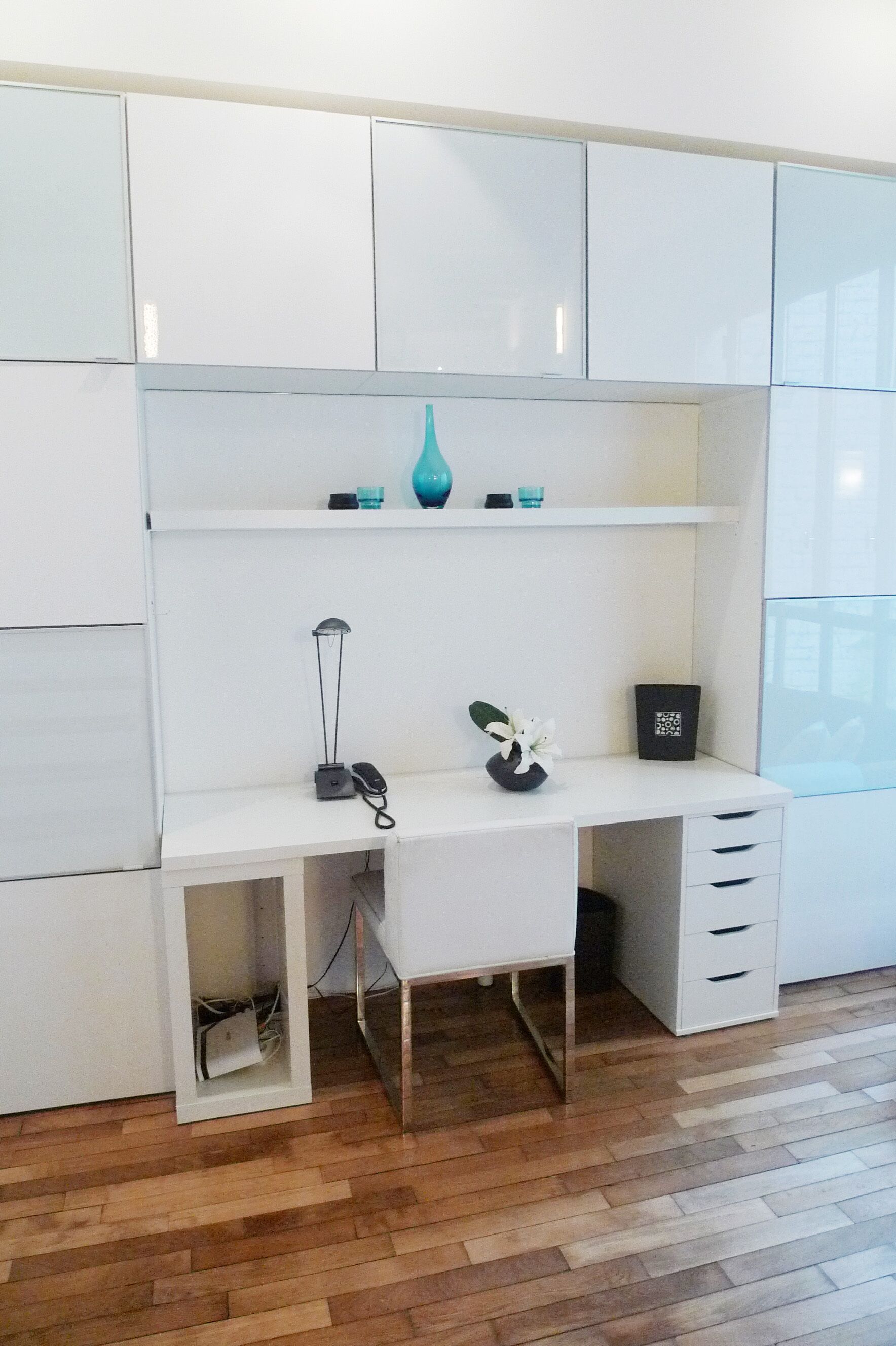 Un espace de bureau moderne avec un bureau blanc, une lampe, un vase et un code QR sur l’étagère.