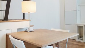 Un pequeño comedor con una mesa de madera y dos sillas blancas, una lámpara y una escalera con vigas a la vista.