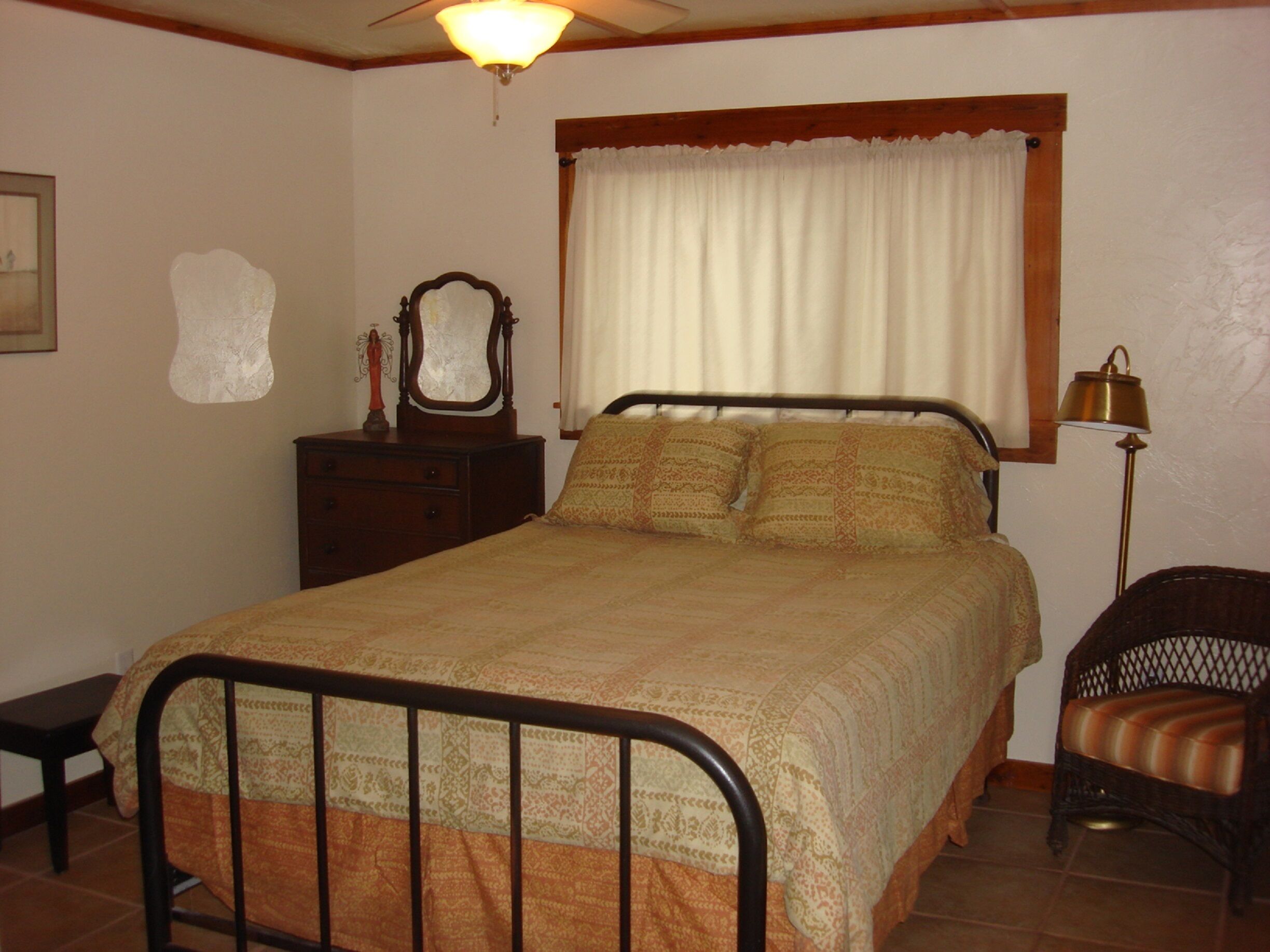 A bedroom with a bed, a dresser, a chair, a lamp, and a window with curtains.