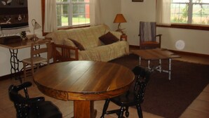 Un salon chaleureux avec un canapé, une table à manger en bois et des chaises. On y trouve des fenêtres avec des rideaux, une lampe et un tableau encadré au mur.