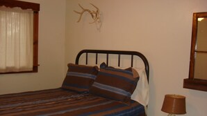 Un lit avec une literie à rayures, une lampe sur une table de chevet et une tête de cerf accrochée au mur.