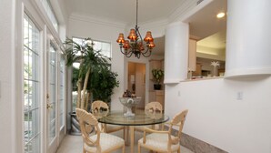 A dining area with a glass table surrounded by four chairs, a chandelier, and a large potted plant. - Pool Compareable to Mirage, Palapa, 82 in Hd TV, Minutes from Strip (Las Vegas)