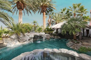 A pool area with palm trees, a waterfall, and a thatched-roof structure. - Pool Compareable to Mirage, Palapa, 82 in Hd TV, Minutes from Strip (Las Vegas)