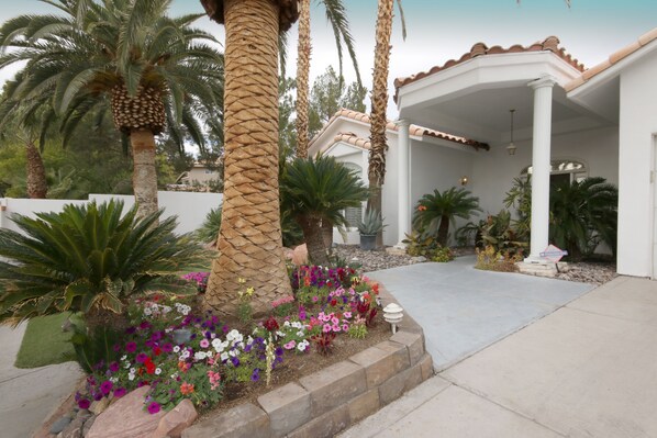 A covered patio area with a concrete floor, surrounded by a variety of plants and flowers. - Pool Compareable to Mirage, Palapa, 82 in Hd TV, Minutes from Strip (Las Vegas)