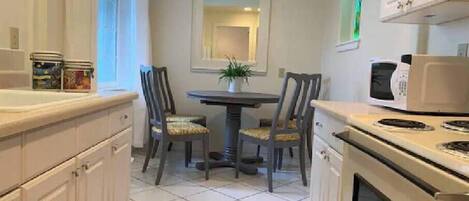 A compact kitchen with white cabinets, a dining table with two chairs, a microwave, and a stove.