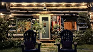 A rustic cabin with a porch, two Adirondack chairs, and an American flag.