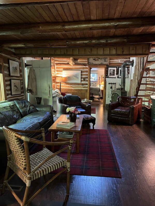 A cozy cabin interior with a wooden ceiling, a fireplace, a sofa, a chair, and a dining table. - Historical Cabin in Good Hart on M119 Tunnel of Trees Lake Michigan Beach Access (Harbor Springs)
