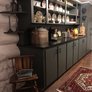 Una cocina con armarios oscuros, una cafetera y una silla de madera con libros.