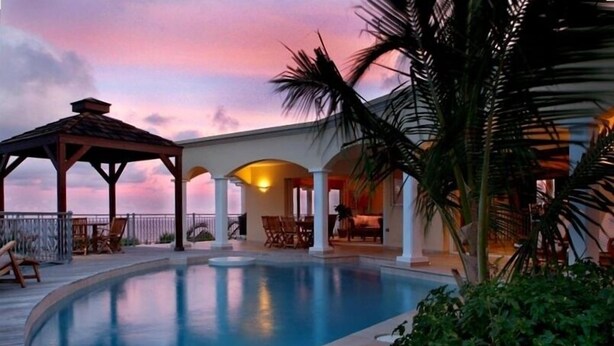 A swimming pool with a covered area and lounge chairs, surrounded by palm trees and a sunset sky. - Luxury Villa w Spectacular Ocean Views, private pool/Hottub, Walk to Beach (Upper Prince's Quarter)