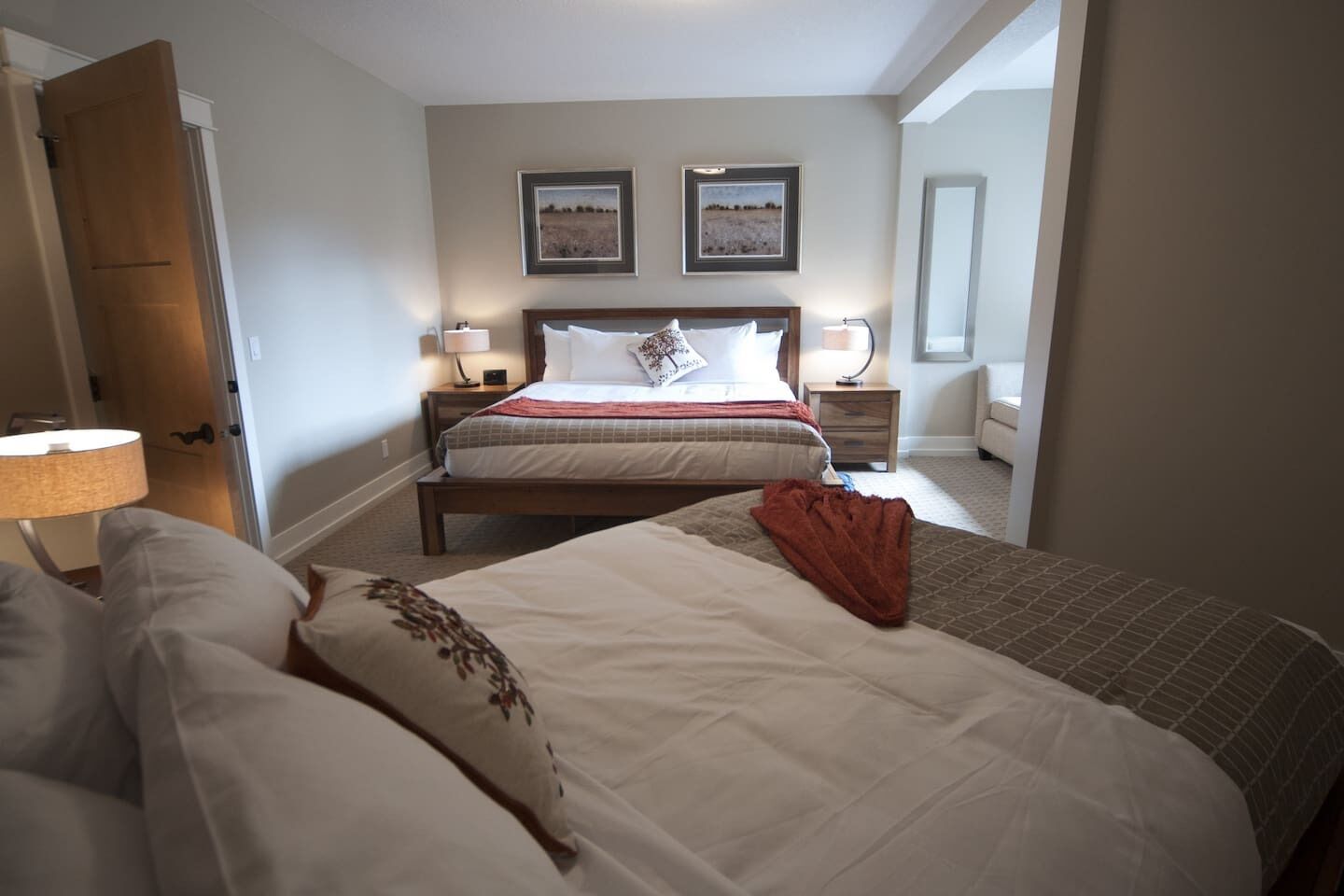 Une chambre d’hôtel avec un grand lit, deux tables de chevet avec des lampes, une porte et deux tableaux encadrés au mur.