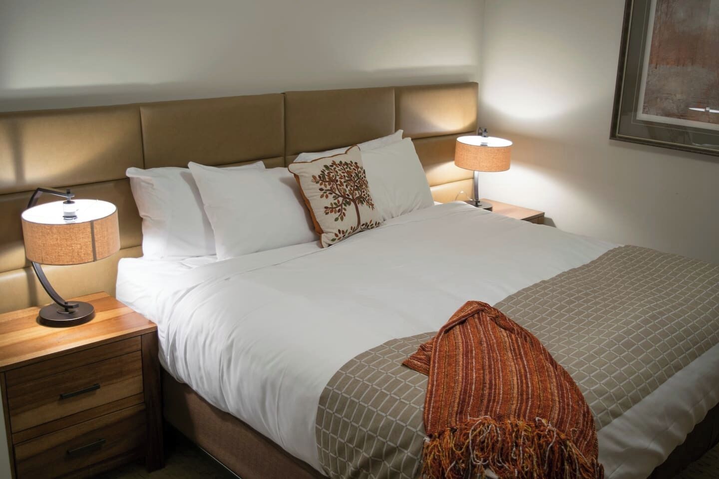 A neatly made bed with white linens, a brown headboard, and two bedside lamps.