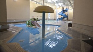 An indoor pool with a slide and a frog statue.