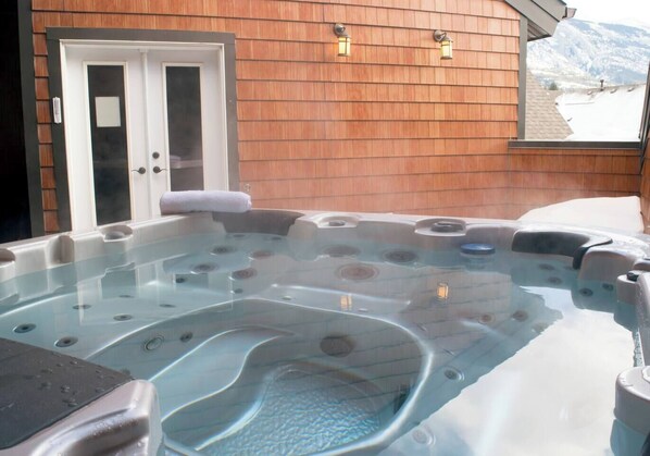 Ein Whirlpool mit Glasumrandung, eine Tür mit Handtuch und eine Holzwand mit zwei Wandleuchten.