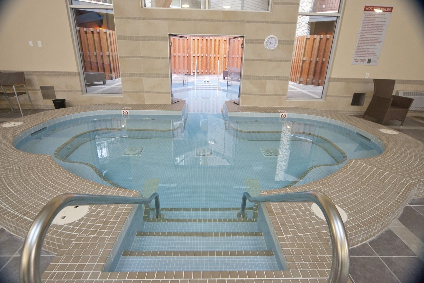 An indoor swimming pool with clear water, tiled steps leading into the pool, and wooden panels in the background.