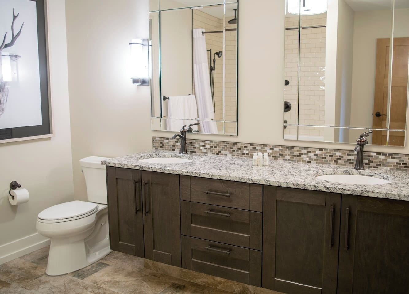 A bathroom with a double sink, dark wood cabinets, a large mirror, and a toilet.