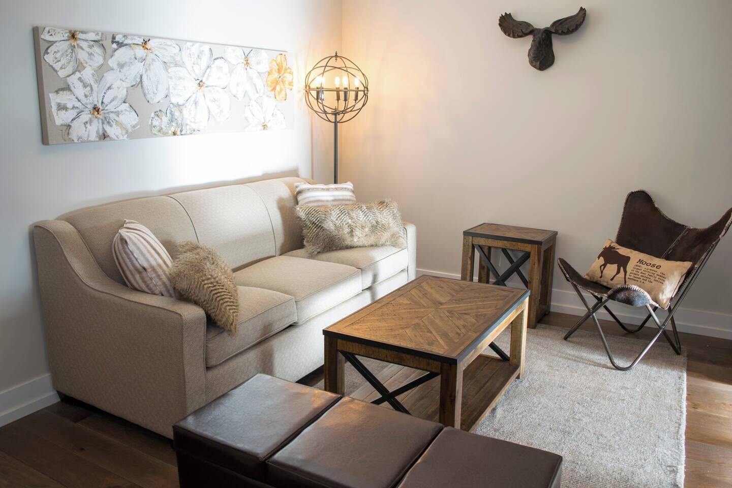 A living room with a sofa, coffee table, ottoman, side table, floor lamp, and a chair with a decorative pillow.