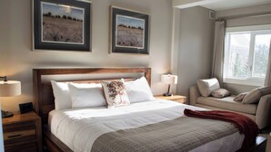A hotel room with a large bed, two bedside tables with lamps, a sofa, and two framed landscape paintings on the wall.