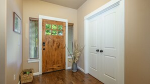 A hallway with wooden flooring, a wooden door, and a white door. There is a basket on the floor and a vase with branches on the right side.