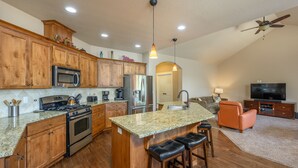 A spacious kitchen with wooden cabinets, a large island with bar stools, stainless steel appliances, and a ceiling fan.