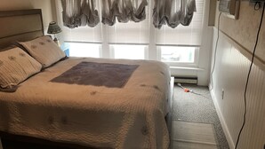 Een slaapkamer met een bed, een raam met gordijnen, een verwarming en een lamp.