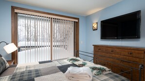 A bedroom with a large bed, a wooden dresser, a flat-screen TV, and a sliding glass door leading to a balcony. - Ski-On/Off - private sauna - right next to lift - 1GB WiFi - Renovated (Killington)
