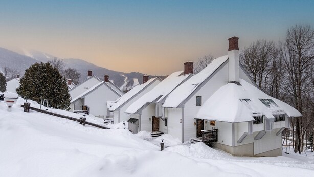 A row of white houses with steep roofs covered in snow, set against a backdrop of mountains and a clear sky. - Ski-On/Off - private sauna - right next to lift - 1GB WiFi - Renovated (Killington)
