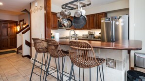 A modern kitchen with stainless steel appliances, a wooden island with bar stools, and hanging pots. - Ski-On/Off - private sauna - right next to lift - 1GB WiFi - Renovated (Killington)