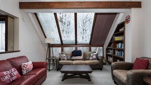 A cozy living room with a red leather sofa, a brown leather armchair, a wooden coffee table, and a bookshelf filled with books. - Ski-On/Off - private sauna - right next to lift - 1GB WiFi - Renovated (Killington)