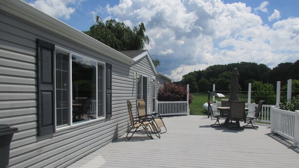 A covered deck with outdoor furniture, a white fence, and a view of a green landscape.