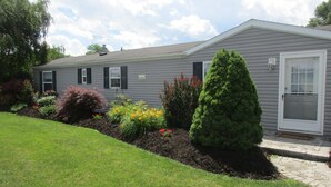 A residential house with a well-maintained lawn, a variety of flowering plants, and a neatly trimmed evergreen tree.