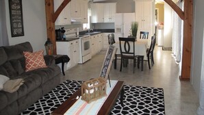 A cozy living room with a sofa and a coffee table, a kitchen with white cabinets and a dining area with a table and chairs.