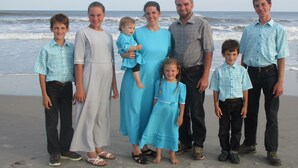 A group of people standing on a beach with the ocean in the background.
